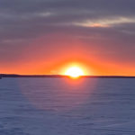 An image of a sunset behind ice huts on frozen Lake Nipissing