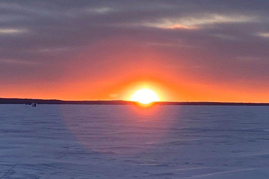 An image of a sunset behind ice huts on frozen Lake Nipissing